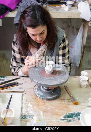 Hand painting the rim decoration on a ceramic jug. A woman worker paints the rim pattern on a piece of pottery at the Ceramica Stock Photo