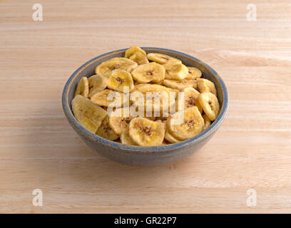 Dehydrated banana chips in an old stoneware bowl atop a wood table. Stock Photo