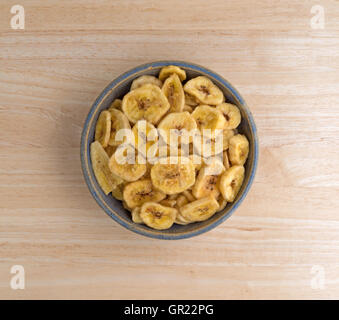 Top view of dehydrated banana chips in an old stoneware bowl atop a wood table. Stock Photo