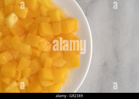 Top close view of diced mangoes on a white plate atop a marble counter top. Stock Photo