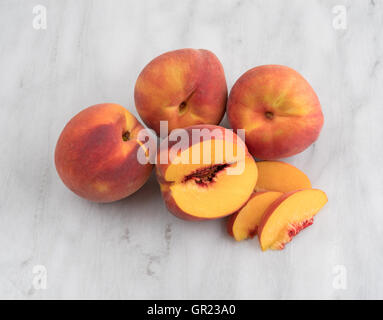 A group of whole nectarines with one slice removed from a fruit on a gray marble cutting board. Stock Photo