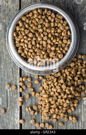 Dried food for dogs or cats in bowl on old wooden table. Top view. Stock Photo