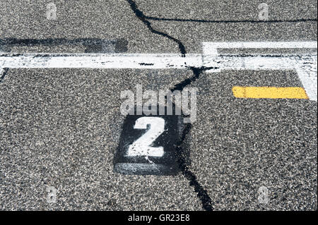Number two position sign on speedway starting track with yellow line and damaged old asphalt Stock Photo