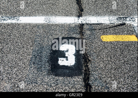 Number three position sign on speedway starting track with yellow line and damaged old asphalt Stock Photo