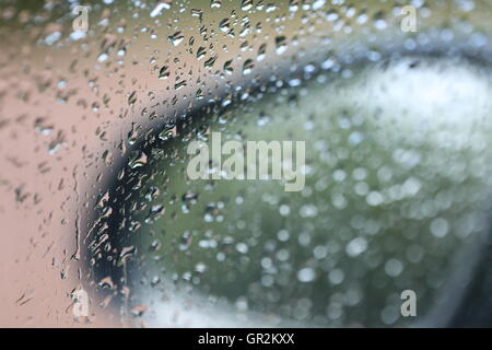 Wet Car Side Mirror. Side mirror of a car through the windshield in the rain. Rain drops on the car glass window. Stock Photo