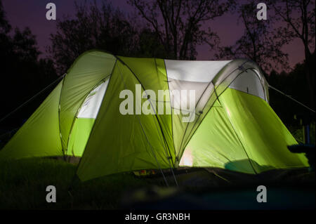 A green and white glowing camping tent is illuminated at dusk in a campground in French Creek State Park pennsylvania Stock Photo