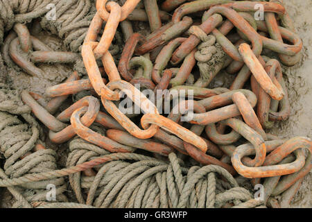 Rusty chain on shingle with muddy rope Stock Photo