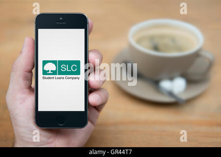 A man looks at his iPhone which displays the Student Loan Company logo, whilst sat with a cup of coffee (Editorial use only). Stock Photo
