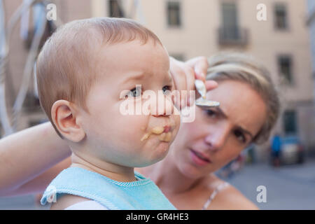 Mother trying to feed her baby boy with fruit mush although he is refusing it Stock Photo