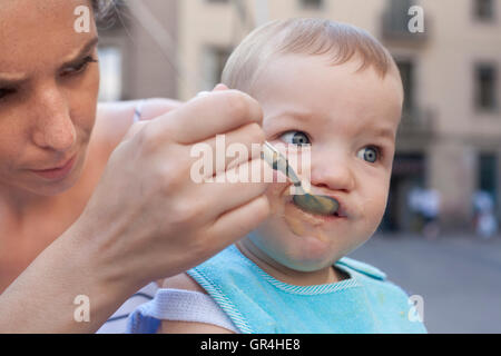 Mother feeding her baby boy with fruit mush outdoors Stock Photo