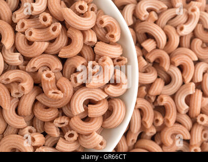 Top close view of red rice elbow shaped pasta in a white bowl surrounded by more food. Stock Photo