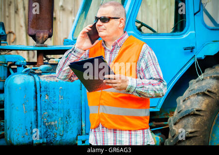 Worker talking on smart phone near tractor Stock Photo