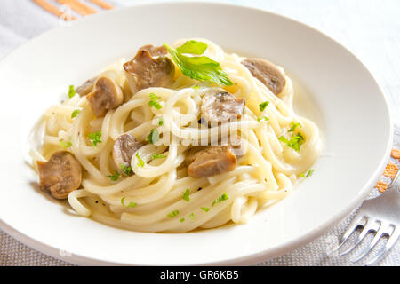 Spaghetti pasta with grilled mushrooms and greens on white plate close up Stock Photo