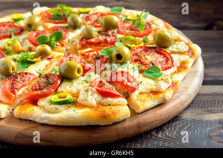 Homemade vegetable pizza with tomatoes, green olives, pepper, basil, oregano and cheese on wooden table with copy space Stock Photo