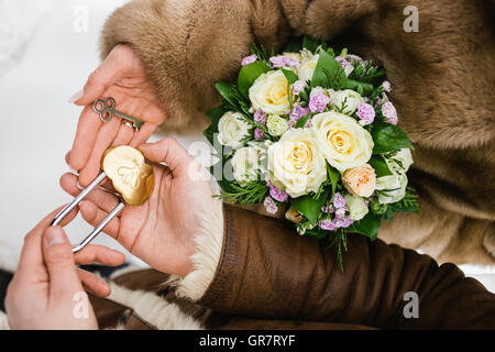 Bridal bouquet and decorative lock with keys on hands. Yellow roses also violet flowers. Winter wedding composition Stock Photo