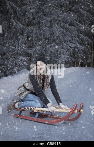 Young Woman Presenting Fall Fashion On Red Sled In Winter Landscape Stock Photo