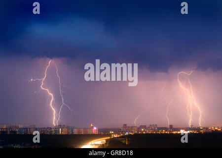 Lightning strike over city in purple light. Stock Photo