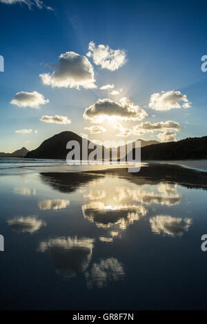 Beautiful ocean sunset. Clouds and sun light reflecting in the water on the beach Stock Photo