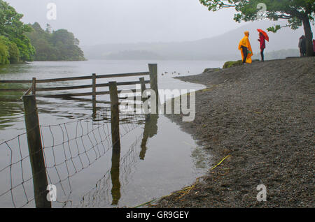 Derwentwater in the rain, two people share a joke under umbrellas, Lake District, UK Stock Photo