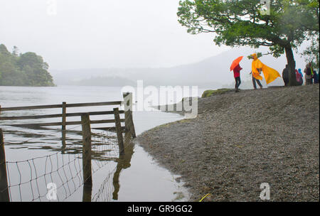 Derwentwater in the rain, two people share a joke under umbrellas, Lake District, UK Stock Photo