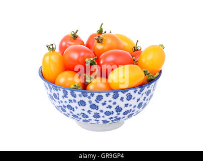 Mixed red and yellow cherry plum tomatoes in a blue and white porcelain bowl with a floral design, isolated on white Stock Photo