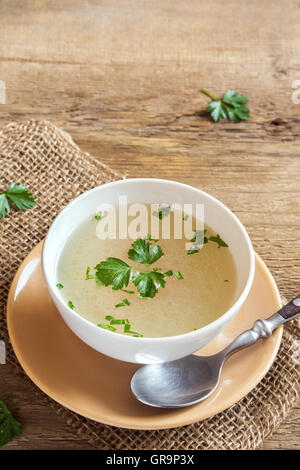 Chicken broth with parsley in white bowl over wooden background with copy space Stock Photo