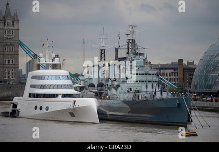 A 390ft motor yacht belonging to Russian tycoon Andrey Melnichenko, alongside HMS Belfast (right) on the River Thames in London. Stock Photo