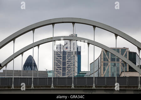 View of the Gherkin and surrounding buildings under cloudy sky framed by arched bridge in London in September Stock Photo