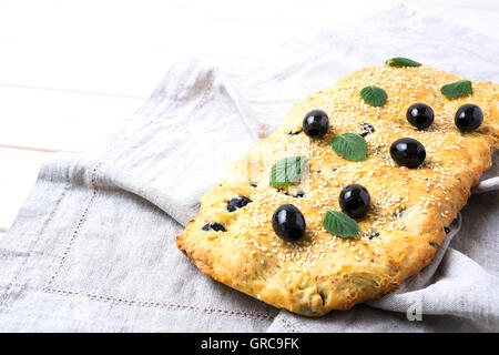 Fresh Italian focaccia with olive, garlic and herbs. Homemade traditional Italian bread on the linen napkin. Stock Photo