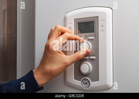Men hand regulate low temperature on 35 degree in control panel of central heating. Stock Photo