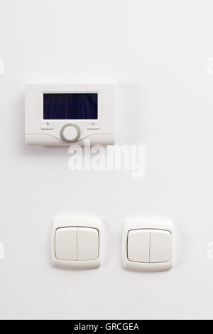 Control panel of central heating and two light switch at white wall on living room. Stock Photo