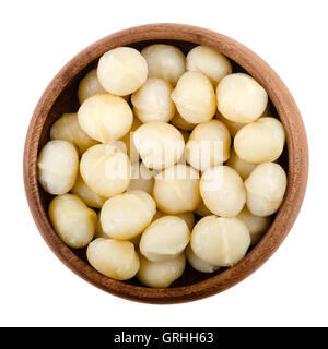 Macadamia nuts in a wooden bowl on white background. Edible seeds without shells. Isolated macro food photo close up from above. Stock Photo