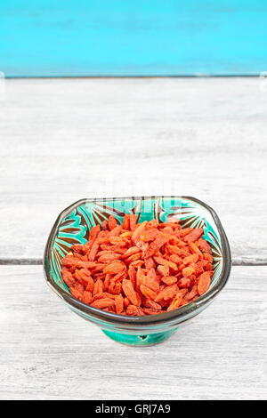Dried goji berries in a green bowl on rustic table, space for text. Stock Photo