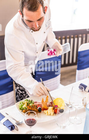 Chef dressed in white uniform decorating appetizer plate with rose petal Stock Photo