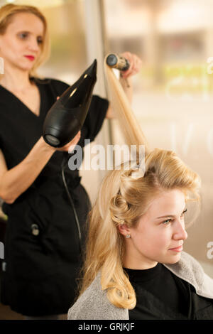professional hair stylist at work - hairdresser  doing hairstyle to  beautiful young blonde customer in a professional studio Stock Photo