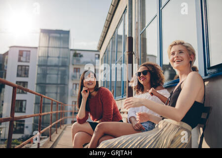 Happy three young female friends sitting in balcony and smiling. Women relaxing outdoors in terrace. Stock Photo