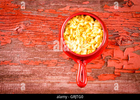Kids cheese macaroni served in glazed clay pot on red rustic picnic table Stock Photo