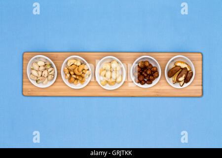 Taster dishes of assorted nuts containing cashews, pistachio, macadamia, hazel and brazil nuts arranged in a row on a wooden boa Stock Photo