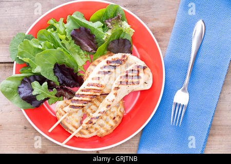 Grilled chicken served with leaf vegetables served on a red plate Stock Photo