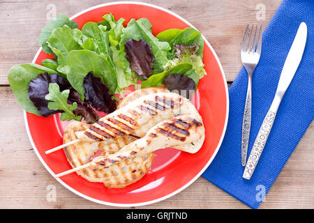 Grilled food served with salad on red plate with fork and knife by its side Stock Photo
