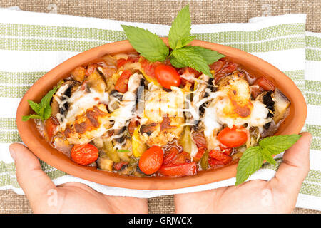 Clean hands are serving chicken stew in stoneware crock pot with a nice clean towel, garnished with mint and topped with mozzare Stock Photo