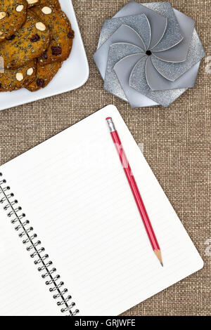 Open blank white notebook with lined pages and a pencil lying on a textured brown cloth with a plate of almond nut cookies and a Stock Photo