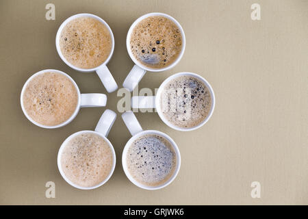 Freshly poured coffee topped with frothy bubbles arranged in a circular radiating design with converging handles on a beige back Stock Photo