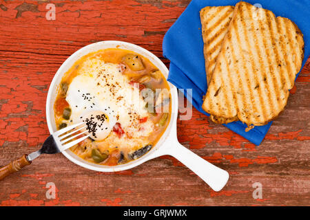 Garden omelet served with bread on a red rustic picnic table with blue napkin and toasted bread Stock Photo