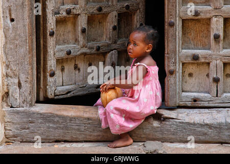 Traditional house with old door and small girl sitting on the street of Stone Town. Stock Photo