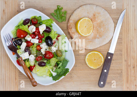 Freshly prepared Mediterranean salad with mixed olives, lettuce, tomato and feta cheese served with lemon for seasoning and fres Stock Photo