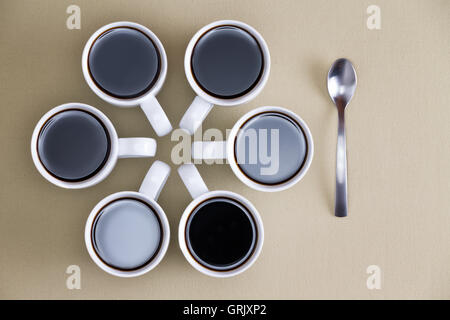 Decorative circular design of coffee mugs full of freshly brewed espresso or filter coffee on beige with converging handles and Stock Photo