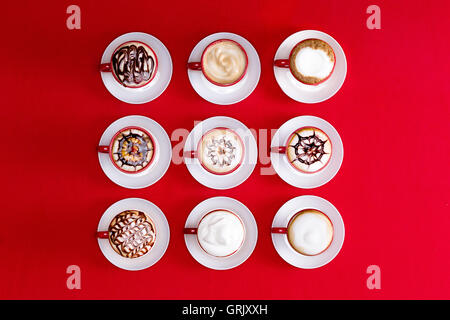 Overhead view of striking patterns and latte art depicted in the foam on espresso or cappuccino coffee in red and white cups and Stock Photo