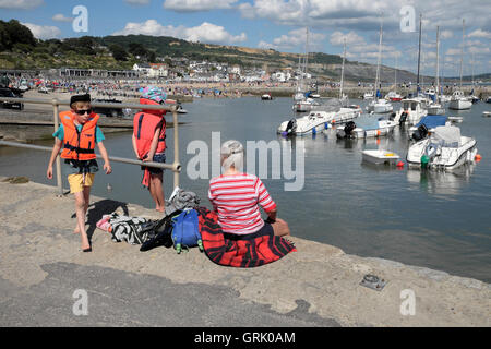 A grandmother and two grandchildren sit on the harbor quay along the Cobb at Lyme Regis Dorset England UK KATHY DEWITT