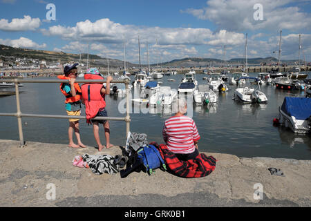 A grandmother and two grandchildren sit on the harbour quay along the Cobb at Lyme Regis Dorset England UK KATHY DEWITT